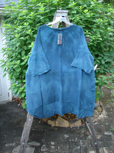 Barclay NWT Crinkle Gauze Ana Tunic Dress in Mottled Teal displayed outdoors on a clothes rack, showcasing its wide three-quarter sleeves, shallow neckline, and varying hemline.