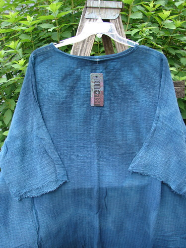 Barclay NWT Crinkle Gauze Ana Tunic Dress Unpainted Mottled Teal OSFA displayed on a wooden stand, showcasing its wide three-quarter sleeves and varying hemline, highlighting its unique, lightweight design.