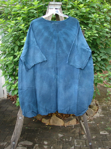 Barclay NWT Crinkle Gauze Ana Tunic Dress in Mottled Teal displayed on a wooden rack, showcasing its wide three-quarter sleeves, shallow neckline, and varying hemline. Perfect condition, lightweight cotton gauze.