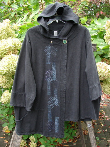 Barclay Fleece Single Button Hooded Jacket Grid Black Size 2 in a cape-like silhouette, featuring wide three-quarter sleeves, cozy hood, ceramic button closure, and patch pockets, set against garden foliage.