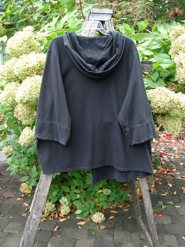A Barclay Fleece Single Button Hooded Jacket Grid Black Size 2 draped over a wooden stepladder in a garden, showcasing its cozy hood, wide sleeves, and unique button closure.