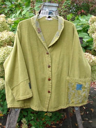 Barclay Patched Flannel Frolic Jacket Green Seed Size 2 features a relaxed, boxy cut with wooden buttons, patch pockets, contrasting patches, and a shawl-style collar, hanging in a garden setting.