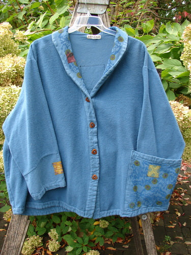 Barclay Patched Flannel Frolic Jacket Garden Blue Teal Size 2 with wooden buttons, patchwork details, and notched collar, displayed on a hanger against green foliage, highlighting its cozy, artistic design.