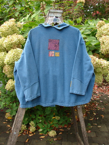 Barclay Patched Flannel Frolic Jacket Garden Blue Teal Size 2 displayed on a wooden ladder, showcasing unique painted patches and oversized pocket, set against a garden backdrop with hydrangeas and fallen leaves.