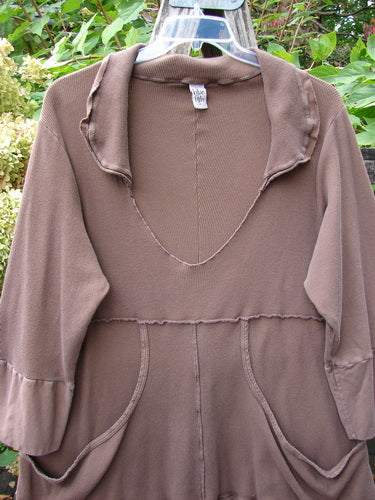 Barclay Thermal Flutter Neck Kangaroo Pocket Top Leaf Mud Size 0, featuring exposed seams, a deep V-neck, dual front pockets, and a painted flutter hemline, hanging against foliage.