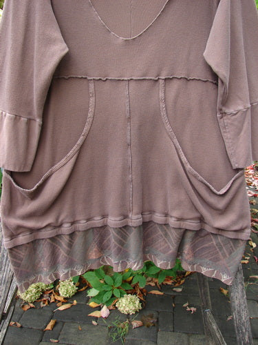 Barclay Thermal Flutter Neck Kangaroo Pocket Top Leaf Mud Size 0, featuring a scooped neckline, long sleeves, dual front patch pockets, and a layered hem revealing a sheer patterned under-layer, draped on a wooden bench.