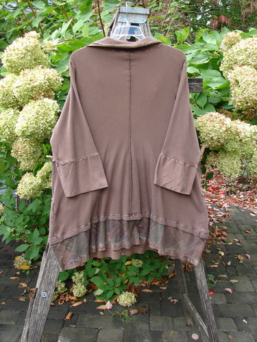 Barclay Thermal Flutter Neck Kangaroo Pocket Top Leaf Mud Size 0 features a loose fit with wide sleeves, a ruffled hem, and cargo pockets, elegantly displayed on a wooden ladder amidst greenery.