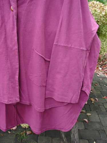 Barclay NWT Reprocessed Golden Hour Jacket, featuring uneven hem, button-down placket, and oversized diagonal pockets, hangs outdoors with hydrangeas in the background. Perfect for expressing individuality.