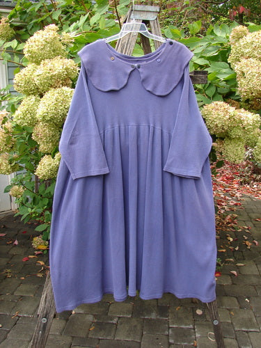 1992 Thermal Silly Collar Dress Unpainted Periwinkle Size 2, featuring an oversized peter-pan collar, hangs elegantly on a wooden ladder amidst garden foliage, showcasing its thermal fabric and sweeping A-line shape.