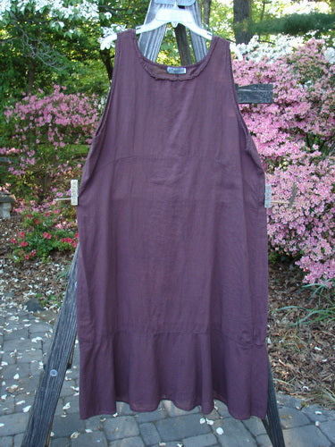 Barclay Batiste Raw Seam Flutter Pinafore Shift Unpainted Fig Size 1 displayed on a wooden ladder, highlighting its wide ruffled lower hem and raw seam rounded neckline.