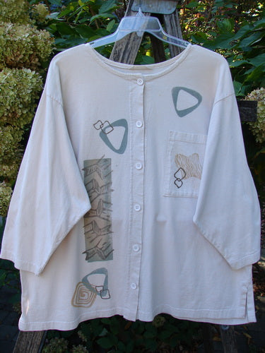 1995 Stargazer Jacket Chair Row China OSFA: Cream button-front blouse with geometric prints, elbow-length sleeves, round neckline, on clear hanger outdoors. Vintage Blue Fish piece with drop shoulders and single painted pocket.