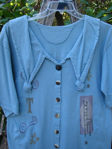 1994 Compass Top Chair Dusk Size 1: Light-blue short-sleeved blouse with mismatched buttons, knot-tied shoulders, swirl and flower prints, and chair motif. Features an over collar and side vents.