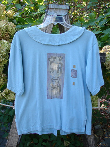 1994 Compass Top Chair Dusk Size 1 hangs on a clear hanger over a wooden ladder. Features include a wide Peter Pan collar, abstract floral graphic, and original buttons.