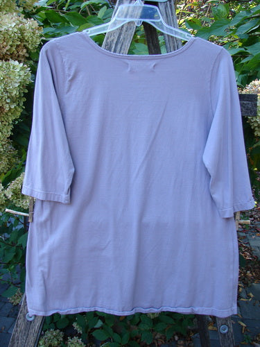 Barclay Three Quarter Sleeved Tee Play Dress Up Lilac Size 1 displayed on a clear hanger, showcasing its mid-weight organic cotton fabric, sweet neckline, and three-quarter sleeves against a garden backdrop.