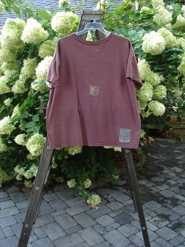 1991 Short Sleeved Tee on a rack. Mulberry color. Mid weight cotton jersey. Billowy sleeves, dropped shoulders. Ribbed neckline. Quiet Thinking Chair theme. Blue Fish Patch. Bust 54, Waist 54, Hips 54. Length 28.