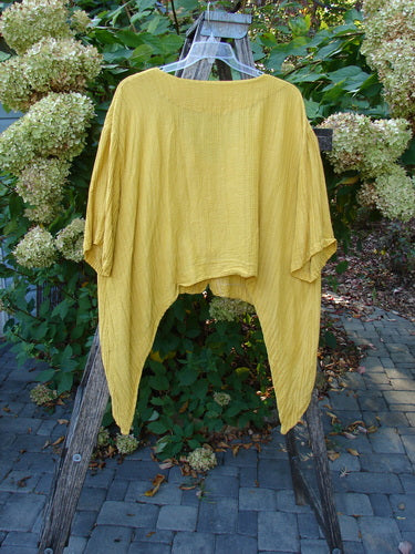 Barclay Rib Silk Dip Side Button Jacket Golden Sunshine Size 1 displayed on a clear hanger against hydrangea bushes, showcasing its loose, drapey silhouette, three-quarter sleeves, and unique hemline.