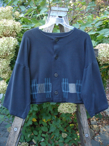 1999 Interlock Side Tie Jacket Fall Grid Black Size 2, featuring a boxy, cropped silhouette with wide, belled sleeves, grid-pattern patches near the hem, and unique rubber buttons, hanging on a garden trellis.