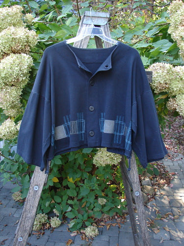 1999 Interlock Side Tie Jacket Fall Grid Black Size 2 displayed on a clear hanger, features a loose, cropped design with wide sleeves, geometric patch accents, and a button-front against a garden backdrop.