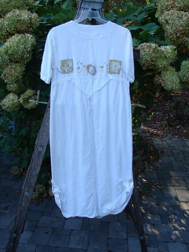 1999 Textured Linen Water Dress Garden Friends White Size 0, displayed outdoors on a wooden trellis. Features include floral appliqués, drawstring accents, empire waist, and pleated front, highlighting Bluefishfinder.com’s vintage charm.