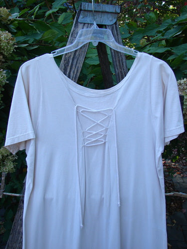 1994 Loop Dress Magic Garden Tea Dye Smaller OSFA: A cream-toned, loose-fitting dress with lace-up neckline, short sleeves, and flared hemline, displayed outdoors on a hanger, highlighting its vintage charm and graceful movement.