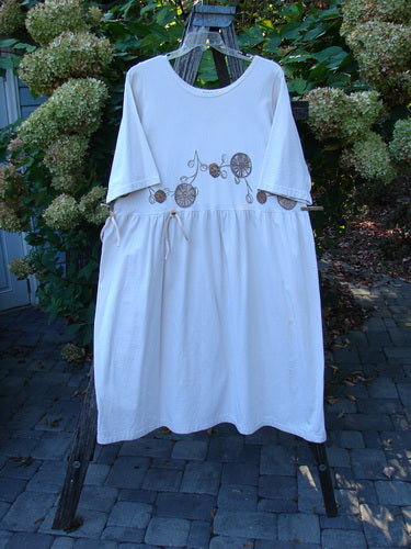 1994 Flower Garden Dress Garden Trail Altered Ecru Size 2, loose-fitting with a round neckline and elbow-length sleeves, features an embroidered motif and gathered waist, displayed on a wooden ladder amidst garden foliage.