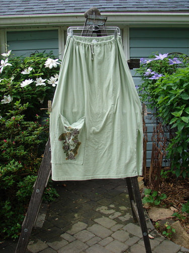 1994 Pocket Skirt Magical Garden Seawater Size 1 displayed on a ladder, showcasing its full A-line shape, single side vent, front pocket with garden-themed paint, and drawcord waistline.