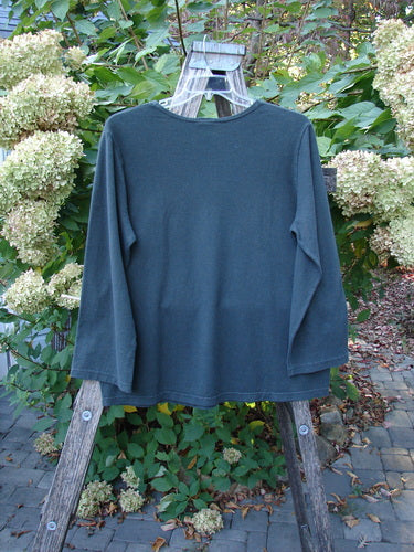 Barclay Hemp Cotton Long Sleeved Tee Unpainted Deep Forest Size 1 displayed on a wooden rack, highlighting its rounded neckline, drop shoulders, and straight elongating shape, set against a garden backdrop.