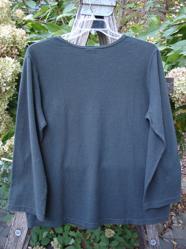 Barclay Hemp Cotton Long Sleeved Tee Unpainted Deep Forest Size 1, hanging on a clear plastic hanger over a wooden ladder, showcasing its drop shoulders, rounded neckline, and straight, elongating shape amidst a garden backdrop.