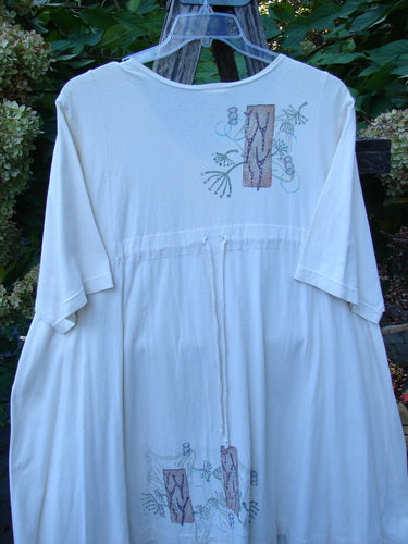 Barclay Tunnel Pocket Pull Over Dress Fish Natural Size 2 features a loose-fitting design with short sleeves, a gathered waist, embroidered earth-tone appliqués, and a front kangaroo pocket, crafted from organic cotton.