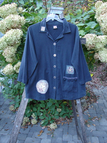 Barclay Patched Flannel PJ Pom Pom Top Pinwheel Black Size 0 on hanger, featuring three-quarter sleeves, notched collar, single patch pocket with floral appliqué, and circular spiral motifs, displayed on wooden ladder.