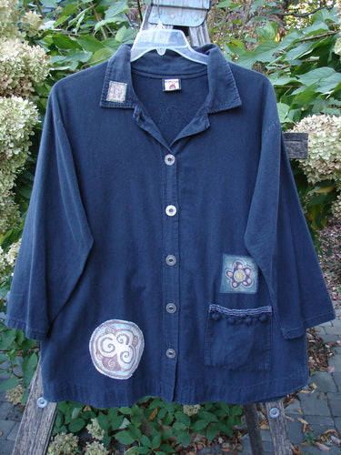 Barclay Patched Flannel PJ Pom Pom Top Pinwheel Black Size 0 on a hanger outdoors, featuring three-quarter sleeves, patch pockets, and decorative appliqué patches, against a backdrop of foliage and hydrangeas.