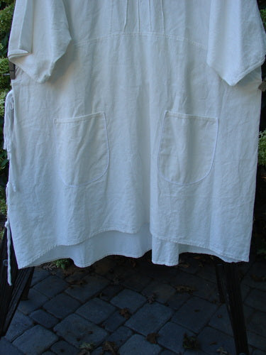 Barclay Linen Duet Sunrise Dress in Crème, displayed on a clothesline, featuring two front pockets, curly cotton neckline, and puckered upper bodice pleats.