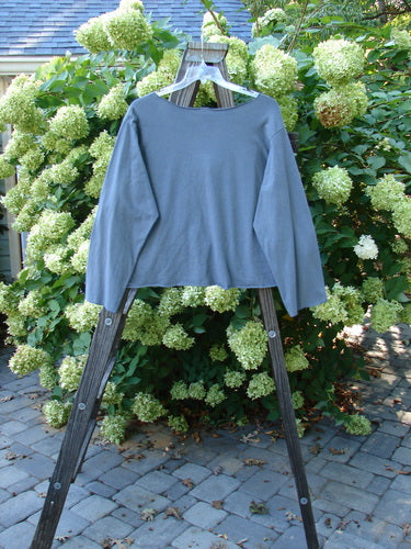 Barclay NWT Layering Cardigan Shrug Rain Flower Blue Dusk Size 2 displayed on a wooden rack, showcasing its long sleeves, open front, and varying hemline with a trailing rain flower theme.