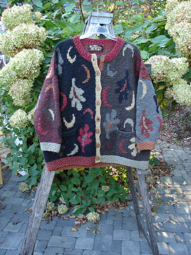 Tara Handknits Star Button Pocket Cardigan Leaf & Moon Brights OSFA draped on a wooden ladder, showcasing its abstract motifs and metal star buttons, embodying luxurious, handcrafted artistry by Hot Knots Sisters.