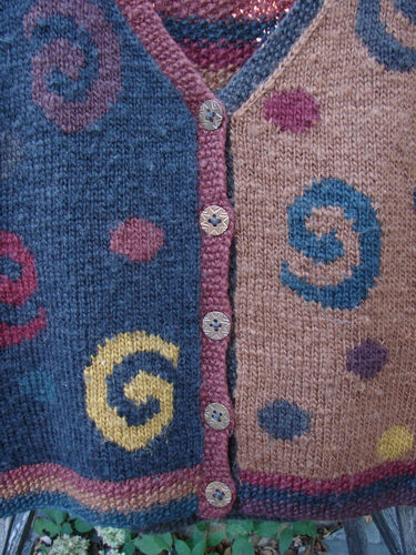 Tara Handknits Back Tab Vest showcases a whimsical swirl-and-dot pattern in bluish and tan hues, adorned with contrasting spiral motifs, pink trim, and star-engraved buttons, reflecting Bluefishfinder's vintage, expressive style.