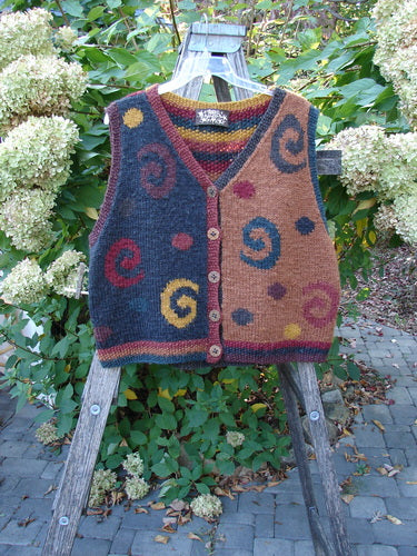 Tara Handknits Back Tab Vest Swirl Polka & Stripe Brights OSFA, featuring bold contrasting color blocks and intricate spiral and dot motifs, displayed on a wooden ladder against flowering hydrangeas.