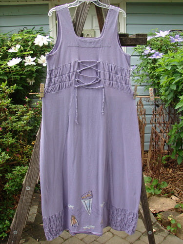2000 Eiffel Dress Spaceship Twilight Size 1 displayed on a wooden rack, showcasing a gathered upper, curved empire waistline, sweeping shape, and unique triangular neckline insert. Made from organic cotton.