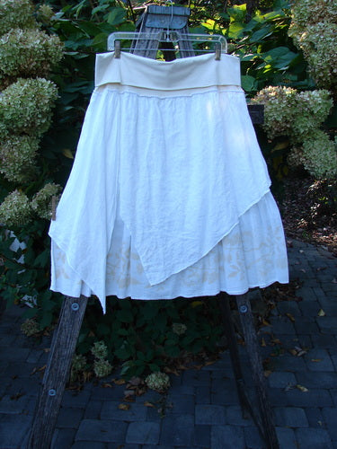 Barclay NWT Linen Fold Over Generosity Skirt hangs on a wooden stepladder, showcasing its asymmetrical draped design and dual-layered batiste with vine and leaf patterns.