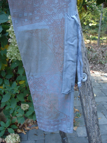 Barclay Cotton Lycra Side Gather Legging Lattice Moss Size 0 draped over a rustic wooden railing, showcasing its intricate geometric print and elastic waistband, amidst a garden backdrop.