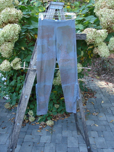 Barclay Cotton Lycra Side Gather Legging Lattice Moss Size 0 hangs on a wooden A-frame ladder, showcasing its slim cut and subtle design against a backdrop of lush hydrangea bushes.