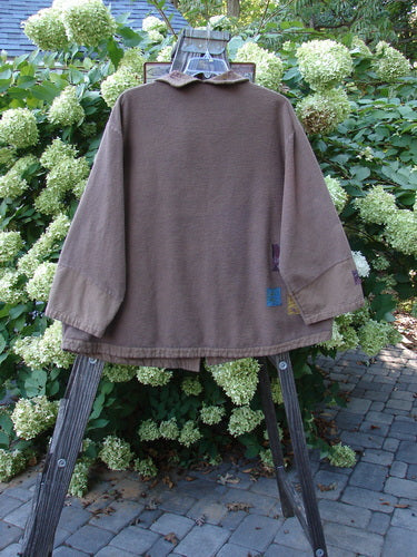 Barclay Patched Flannel Frolic Jacket Vine Garden Rock Size 2 displayed on a wooden stand, showcasing its ribbed corded outer, unique buttons, oversized front pocket, and vine garden-themed painted patches.