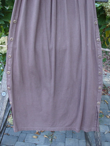 Barclay Button Panel Skirt Vegetable Sepia Size 2 drapes elegantly over a wooden bench, showcasing its side seam buttons and painted front panel, reflecting the store’s vintage and creative ethos.