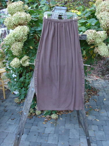 Barclay Button Panel Skirt Vegetable Sepia Size 2 displayed on a wooden trellis, showcasing elastic waistband and decorative side buttons, in a picturesque garden setting.