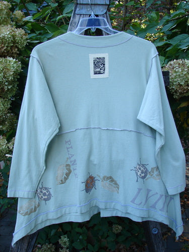 1998 Botanicals Orchard Jacket Plante Grasshopper Altered Size 1 features a pastel-green tunic with leaf and ladybug designs, pearl buttons, and signature patch, elegantly draped over a wooden trellis.