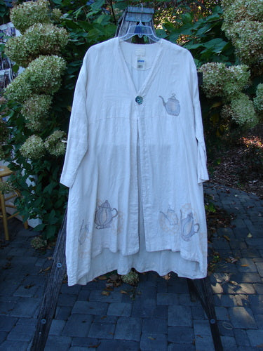 1999 NWT Cream and Sugar Coat Tea Time Teadye OSFA, a knee-length linen smock with teapot appliqués and oversized shell button, displayed on a hanger over a wooden ladder.
