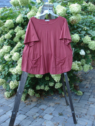 Barclay Double Pocket Twinkle Top Unpainted Cinnabar Size 2 on a wooden stand, showcasing short wider sleeves, a slight boat neckline, and double lower drop exterior pockets in an outdoor setting.