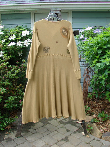 1995 Thermal Soliloquy Dress in Architectural Burnished Gold, displayed on a swing, showcasing its long, sweeping hemline and ribbed sleeves, accentuated by abstract architectural patterns.