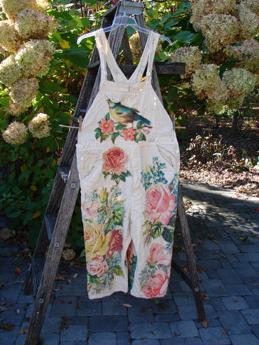 Magnolia Pearl Applique Benjamin Overall Birdie Bouquet Moon OSFA, featuring colorful floral and bird motifs on light‐cream canvas overalls, displayed on a wooden stepladder against a leafy backdrop.
