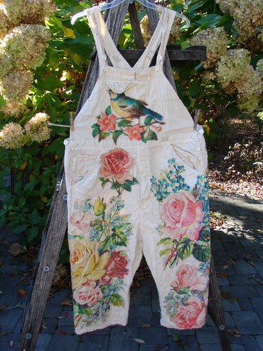 Magnolia Pearl Applique Benjamin Overall Birdie Bouquet Moon OSFA features light cotton overalls with large floral prints and a bird on the bib, hanging on a ladder with greenery behind.