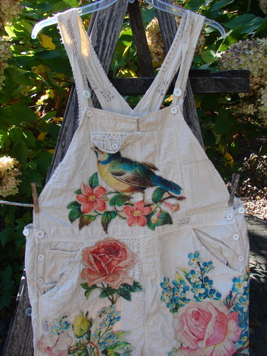 Magnolia Pearl Applique Benjamin Overall Birdie Bouquet Moon OSFA features a light-beige cotton denim with colorful floral motifs and a small bird. Detailed with pockets, adjustable waistline, and distressed finish.